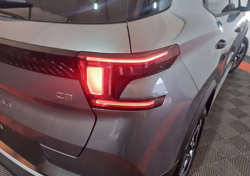 Feu arrière droit allumé d'une Citroën C3 hybride gris foncé vue en 3/4 arrière droit sur sol à motifs.