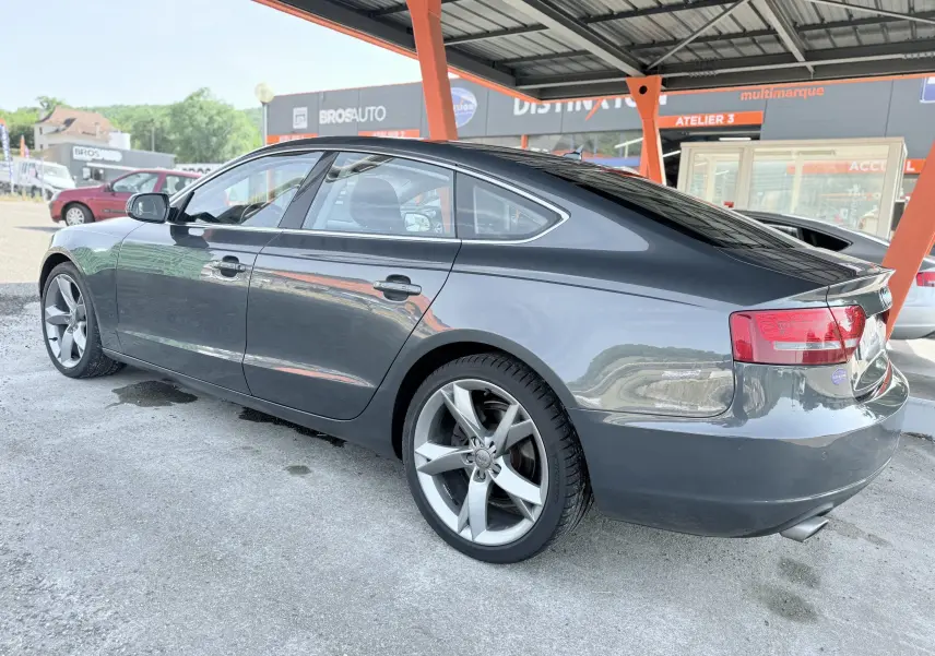 Audi A5 Sportback gris dauphin vue 3/4 arrière côté droit, jantes alliage et feux arrière distinctifs visibles.