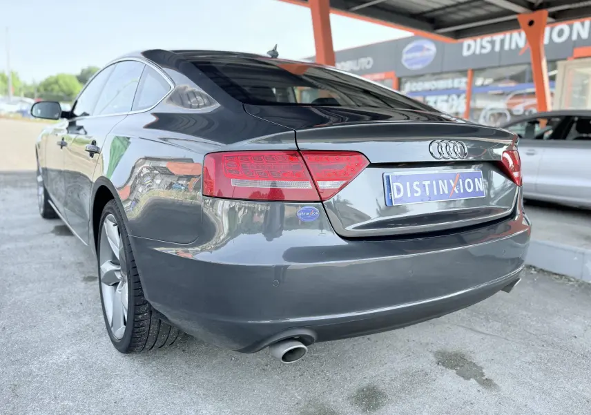 Vue 3/4 arrière droite de l'Audi A5 Sportback gris dauphin 2009 avec feux rouges et sortie d'échappement visible.