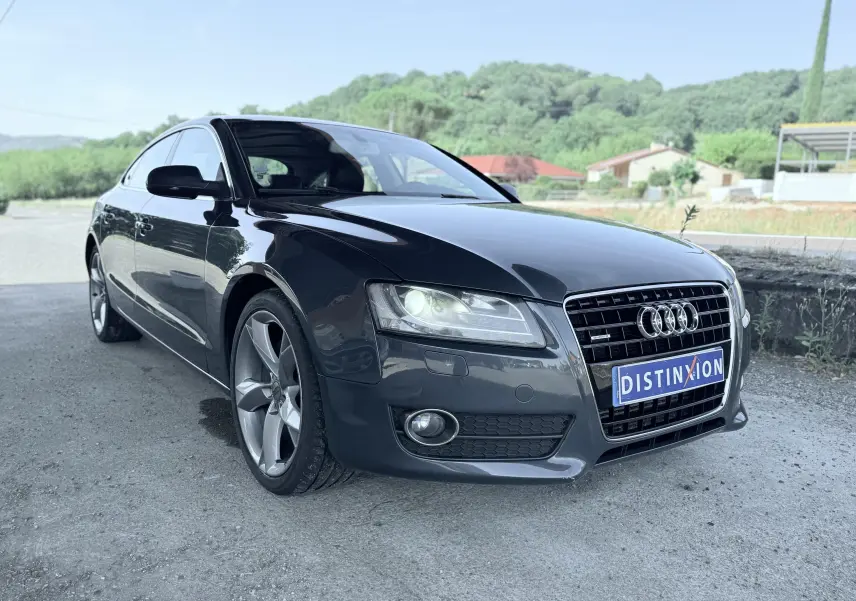 Audi A5 Sportback gris dauphin vue 3/4 avant droit, avec calandre noire et jantes alliage cinq branches.