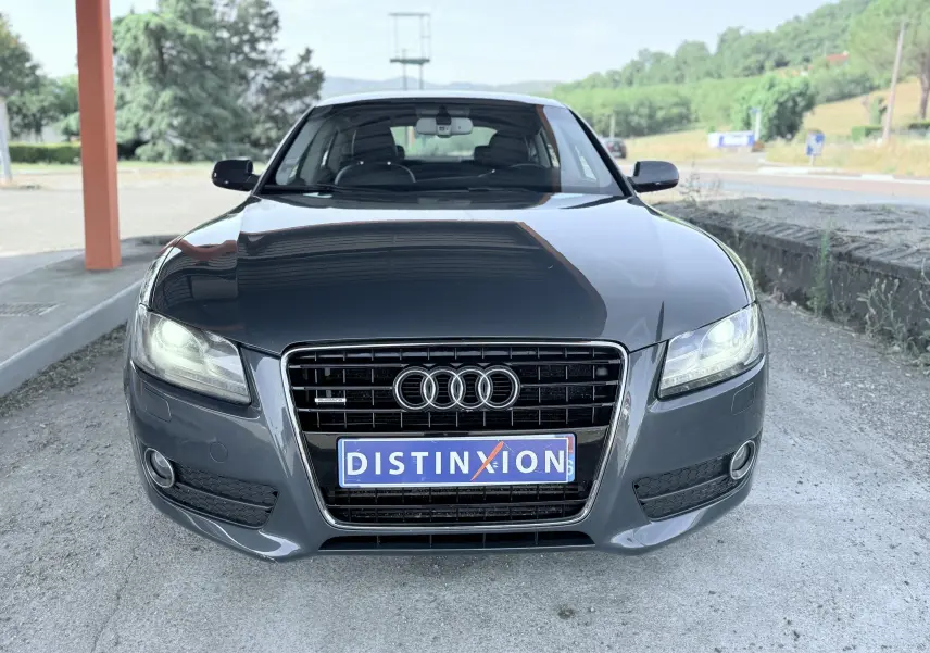 Vue avant d'une Audi A5 Sportback gris dauphin de 2009 avec calandre distinctive et phares allumés.