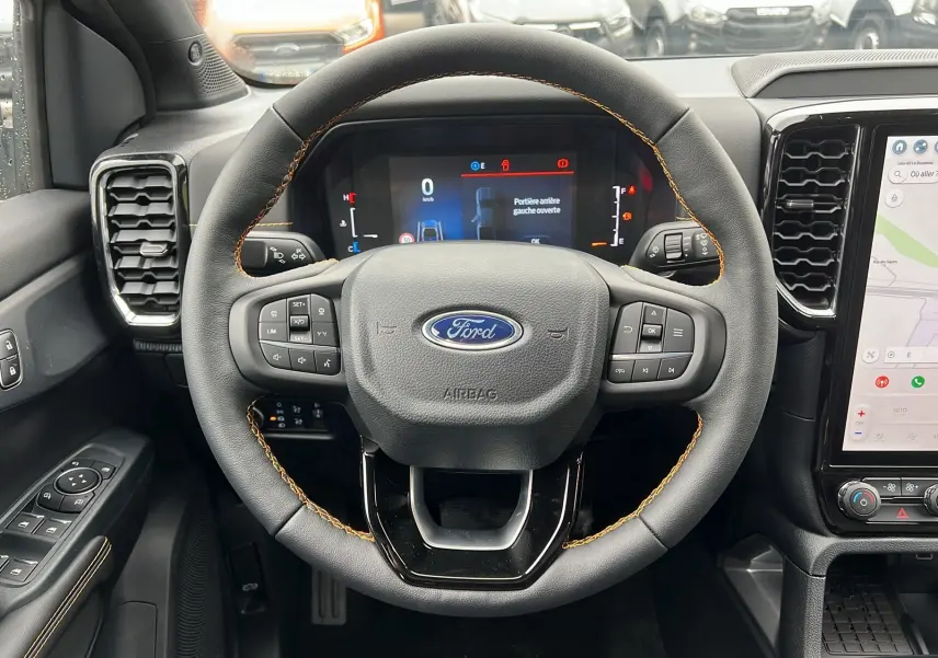 Vue intérieure centrée sur le volant noir avec surpiqûres orange du Ford Ranger 2025 gris carbone, affichage numérique visible.