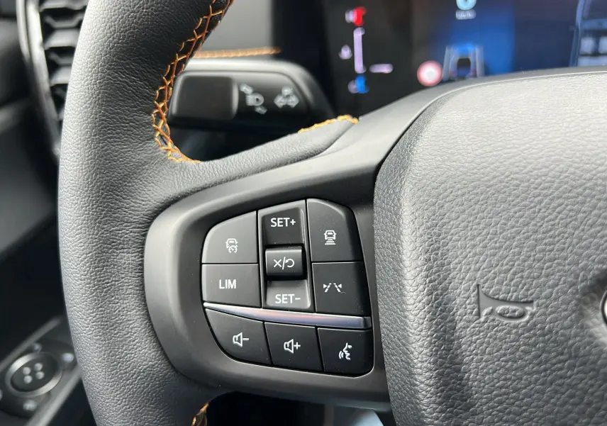 Gros plan sur le volant noir avec surpiqûres orange du Ford Ranger 2025 Wildtrak Plus, montrant les commandes intégrées.