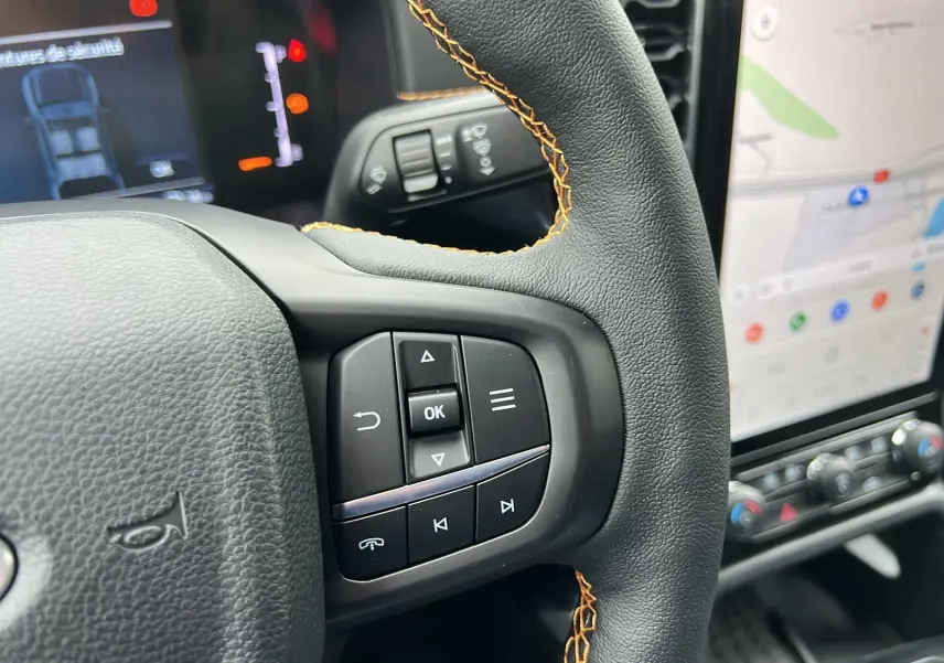 Gros plan sur la partie droite du volant en cuir noir avec surpiqûres orange du Ford Ranger Wildtrak Plus 2025.