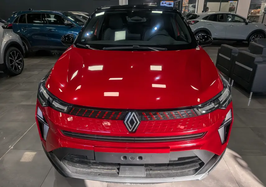 Vue avant d'un Renault Captur 2025 rouge flamme avec toit noir, mettant en valeur sa calandre lumineuse distinctive.