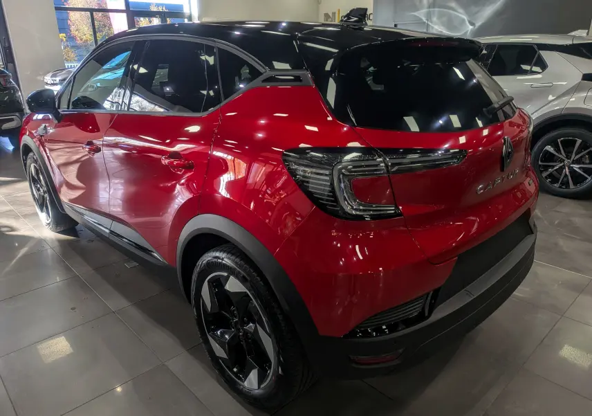 Vue 3/4 arrière droite du Renault Captur E-TECH 2025 rouge flamme avec toit noir et jantes noires en showroom.