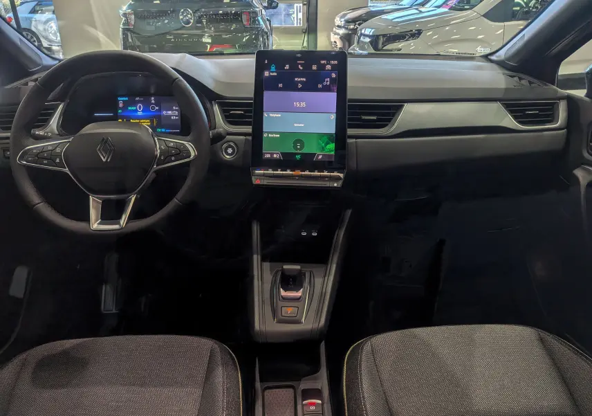 Vue intérieure frontale du tableau de bord du Renault Captur E-Tech 2025 avec écran tactile vertical et volant multifonction.