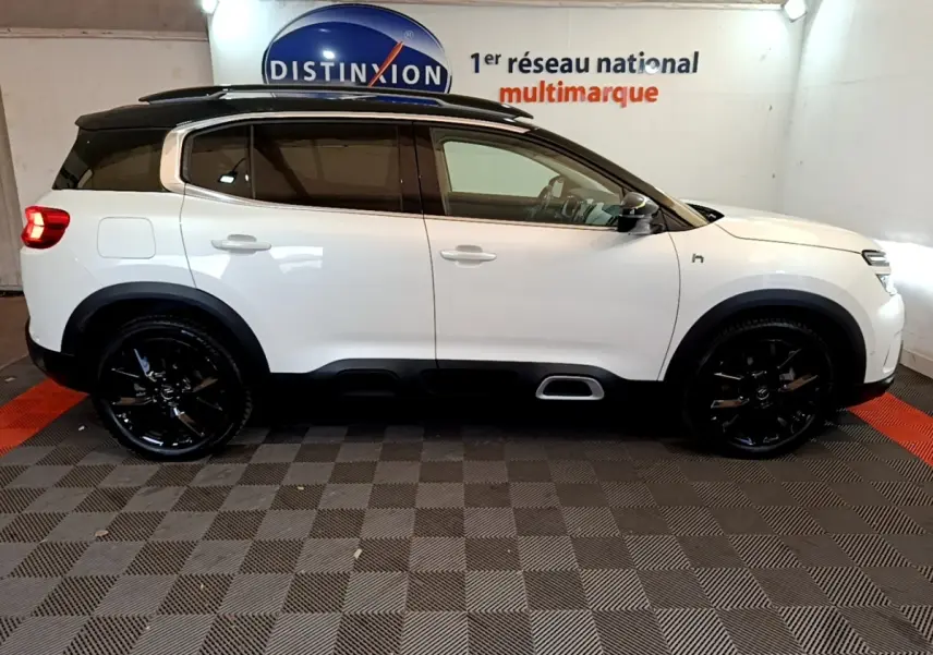 Profil droit d'un Citroën C5 Aircross blanc avec toit noir et jantes noires brillantes dans un showroom.
