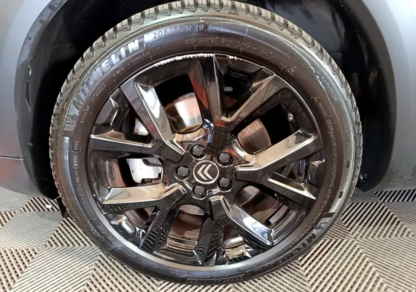 Gros plan sur la roue noire brillante avec logo Citroën, montée sur un Citroën C5 Aircross blanc hybride.