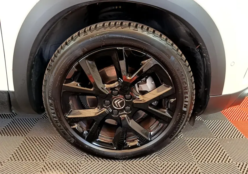 Gros plan sur la roue avant droite noire brillante d'un Citroën C5 Aircross blanc, avec logo Citroën au centre.