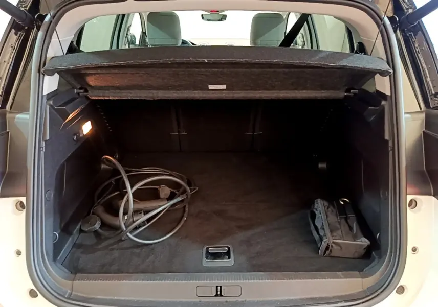 Vue arrière du coffre ouvert d'un Citroën C5 Aircross hybride blanc avec câble de recharge et sac noir à l'intérieur.