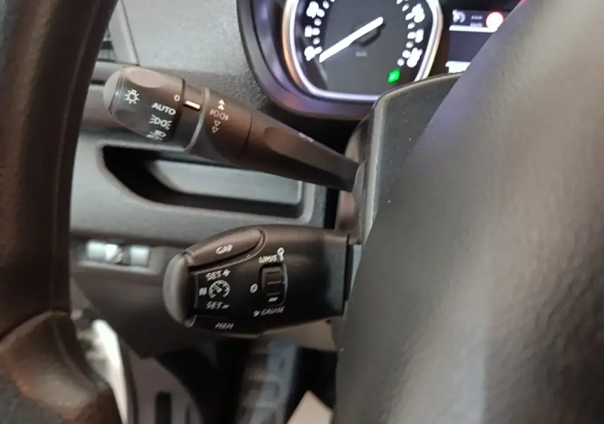 Gros plan sur les commandes du régulateur de vitesse et des feux derrière le volant noir du Peugeot Expert Fourgon blanc.