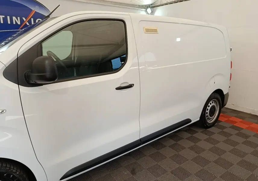 Vue de profil côté gauche d'un Peugeot Expert Fourgon blanc stationné sur un sol à damiers gris et orange.