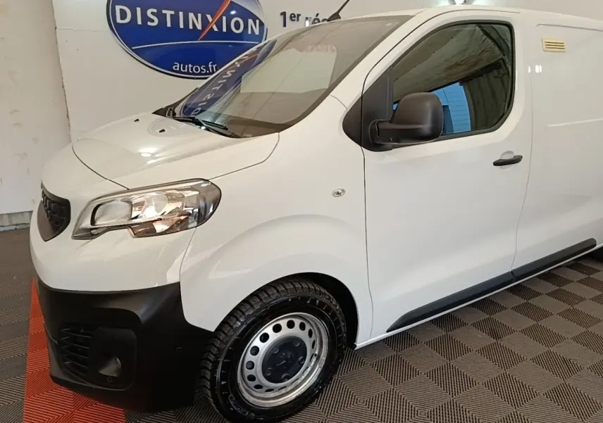 Vue 3/4 avant droit d’un Peugeot Expert Fourgon blanc avec pare-chocs noir et jantes acier en intérieur showroom.
