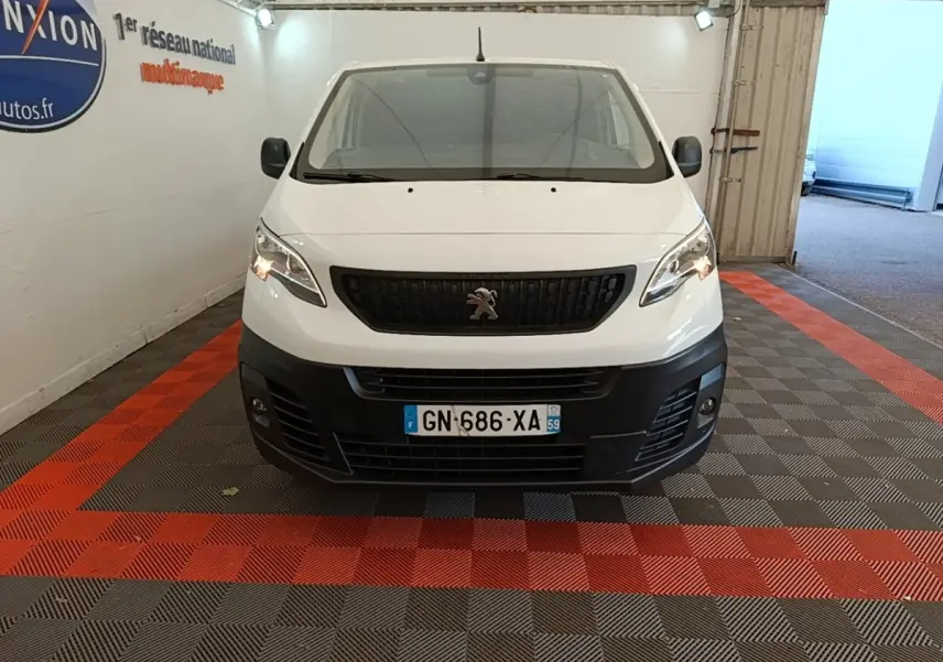 Vue frontale d’un Peugeot Expert Fourgon blanc 2023 avec calandre noire et pare-chocs avant noir dans un garage.