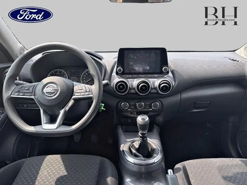 Vue intérieure avant du Nissan Juke 2023 avec volant multifonction, tableau de bord noir et levier de vitesse manuel.