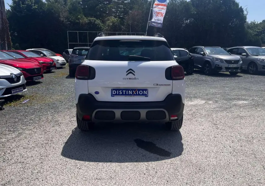 Vue arrière d'un Citroën C3 Aircross blanc Banquise avec barres de toit et feux arrière foncés sur parking.