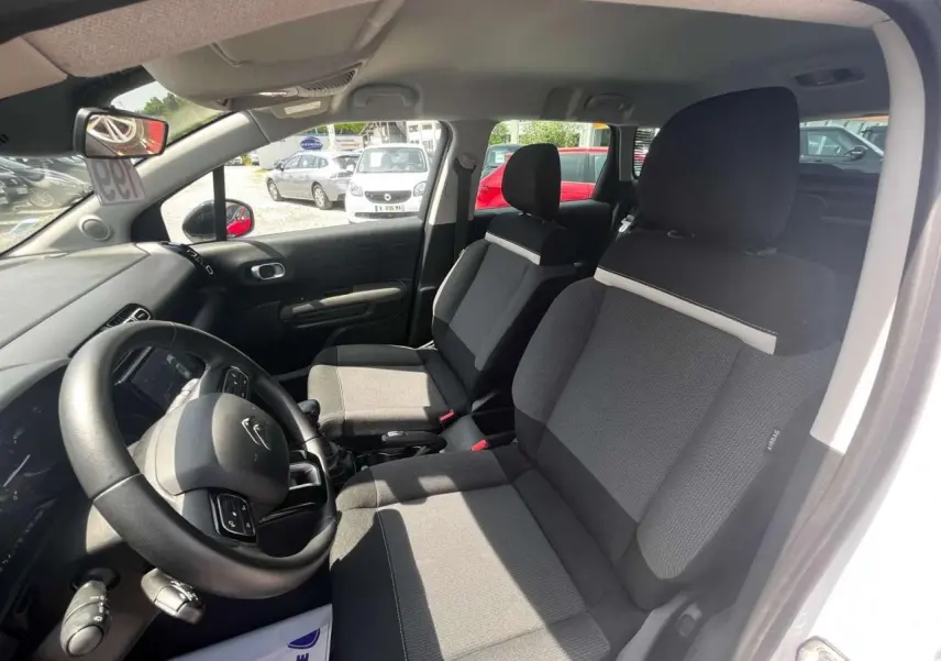 Vue intérieure côté conducteur du Citroën C3 Aircross blanc banquise, sièges tissu gris et volant multifonction.