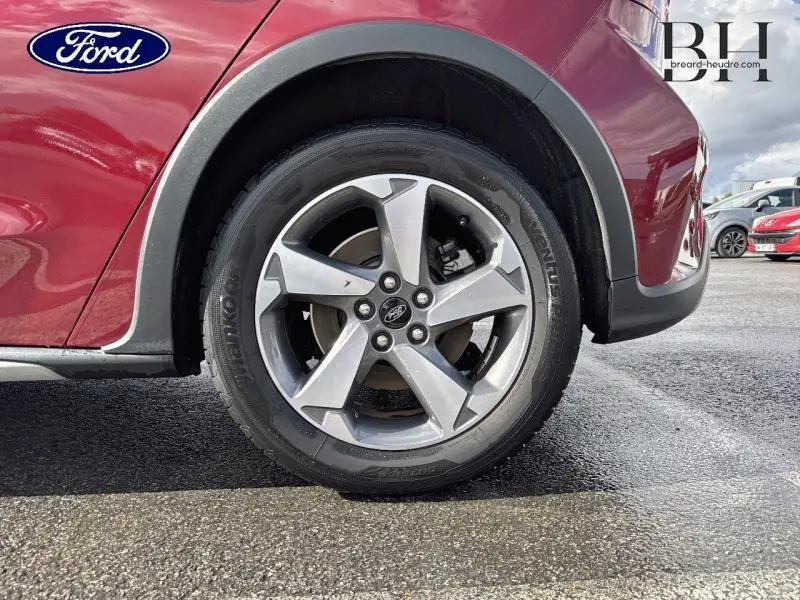 Gros plan sur la roue avant gauche en jante alu d'une Ford Focus 1.0 EcoBoost rouge Premium Candy, avec passage de roue noir.