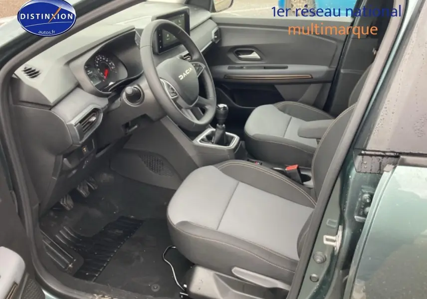 Intérieur avant droit du Dacia Jogger vert cèdre 2025, avec volant, sièges gris et boîte manuelle visible.