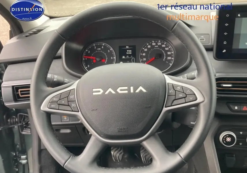 Vue intérieure centrée sur le volant DACIA du Jogger 2025 avec commandes intégrées et tableau de bord visible.