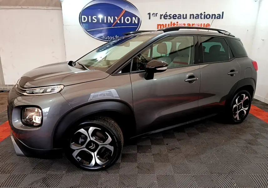 Vue 3/4 avant droit d'un Citroën C3 Aircross gris foncé avec jantes distinctives et barres de toit noires.