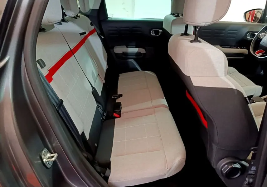 Vue intérieure côté gauche montrant la banquette arrière beige avec bande rouge du Citroën C3 Aircross gris foncé.