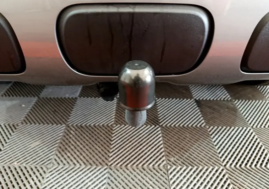 Gros plan sur l'attelage arrière métallique d'un Citroën C3 Aircross gris foncé, posé sur un sol à motifs géométriques.