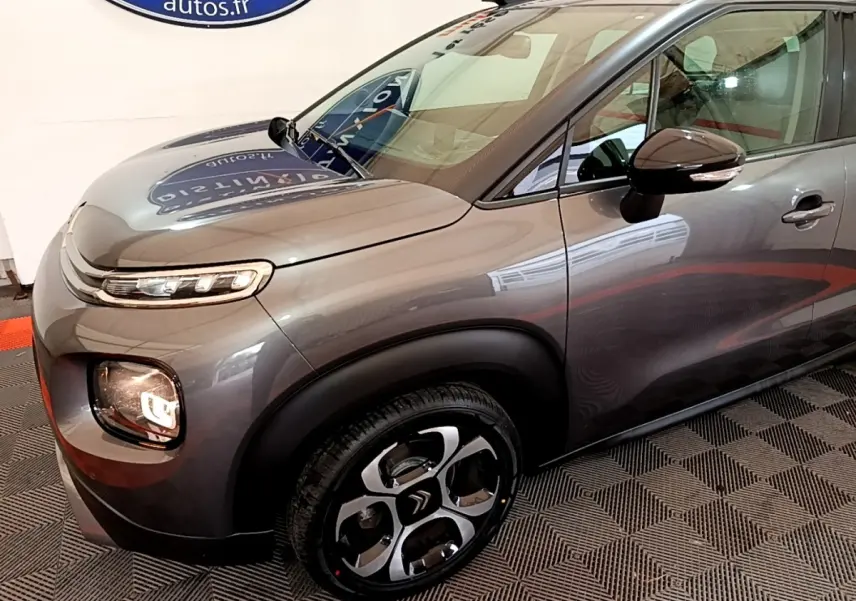 Vue 3/4 avant droit d’un Citroën C3 Aircross gris foncé avec jantes distinctives et rétroviseur noir brillant.