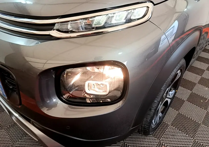 Gros plan sur l'avant droit gris foncé du Citroën C3 Aircross 2020, mettant en valeur ses phares allumés et sa calandre.