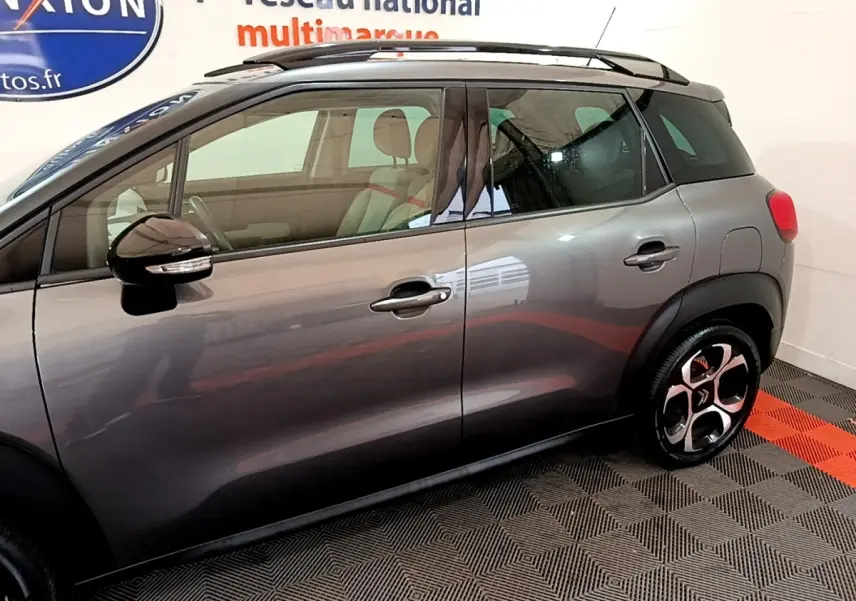 Vue de profil côté gauche d'un Citroën C3 Aircross gris foncé avec toit noir et jantes distinctives.