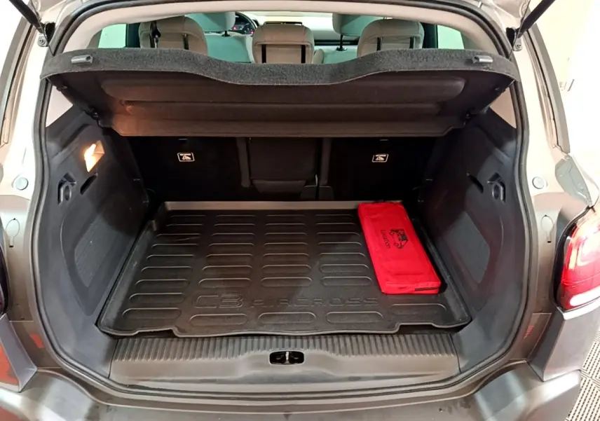 Coffre ouvert d’un Citroën C3 Aircross gris foncé, vue arrière avec tapis de coffre et trousse rouge visible.