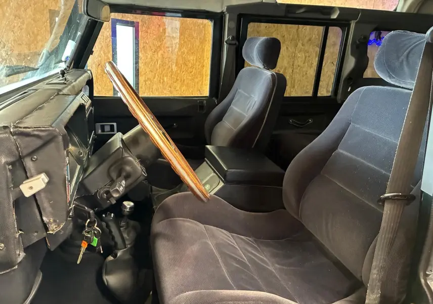 Vue intérieure côté conducteur du Land Rover Defender 110 2005, avec volant bois et sièges noirs en tissu.