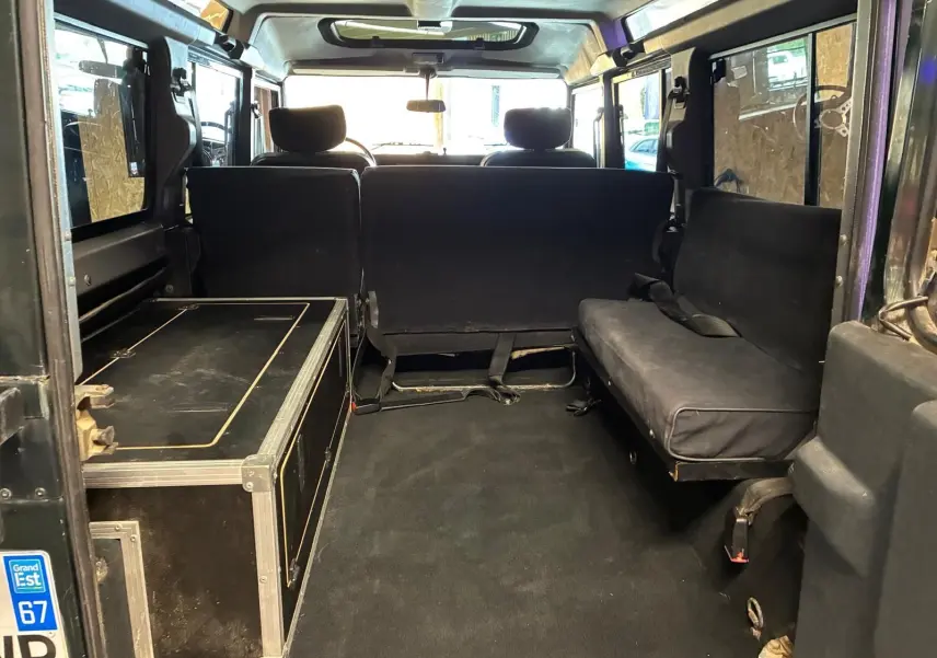 Vue intérieure arrière du Land Rover Defender 110 vert de 2005, montrant les sièges latéraux et un coffre noir.