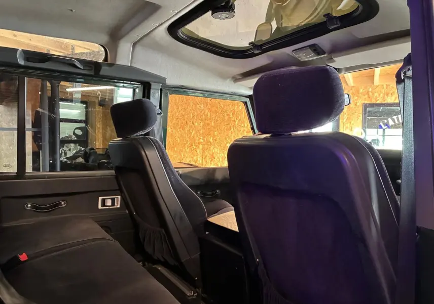 Intérieur arrière du Land Rover Defender 110 2005, vue côté gauche, sièges noirs et toit ouvrant visible.