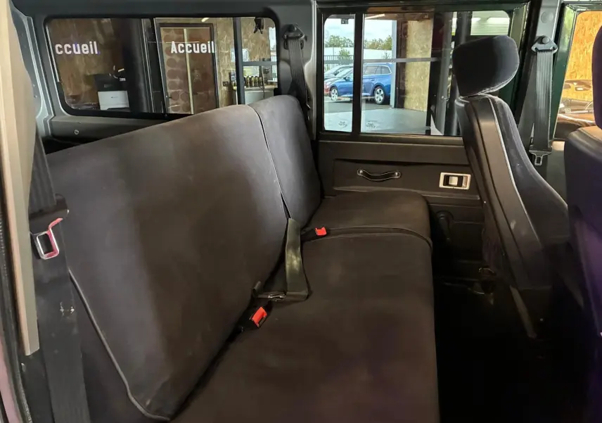 Vue intérieure côté gauche sur la banquette arrière noire du Land Rover Defender 110 vert de 2005.