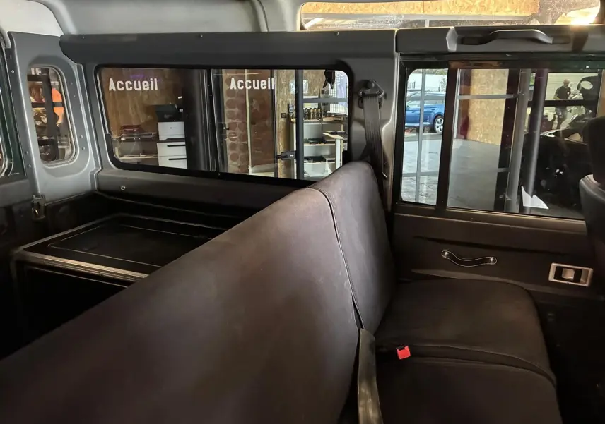 Vue intérieure côté droit du Land Rover Defender 110 vert de 2005, montrant la banquette arrière et les vitres coulissantes.