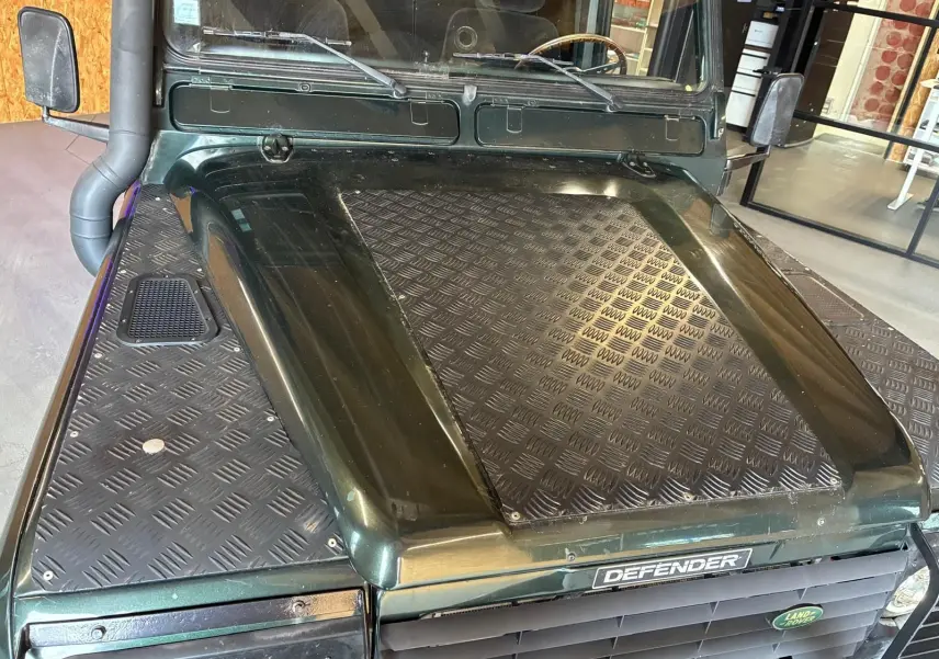Vue avant rapprochée du Land Rover Defender 110 vert 2005, avec capot renforcé en tôle striée et calandre noire.