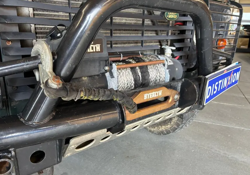 Gros plan sur le treuil avant noir et la calandre verte du Land Rover Defender 110 2.5 TD 122 4x4 de 2005.