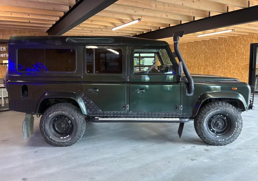 Vue de profil côté gauche d'un Land Rover Defender 110 vert 2005 avec pneus tout-terrain et snorkel noir.