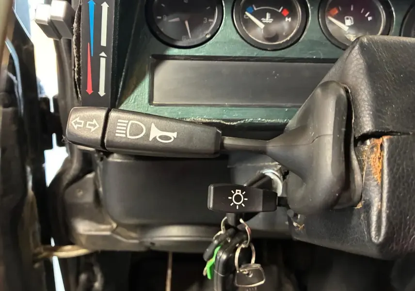 Détail du tableau de bord vert du Land Rover Defender 110 2005, avec manette de clignotants et clés sur le contacteur.