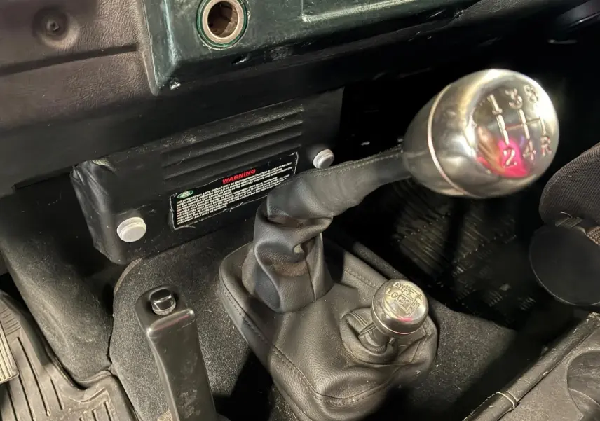 Gros plan intérieur sur le levier de vitesses manuel et le levier de blocage de différentiel du Land Rover Defender 110 vert de 2005.