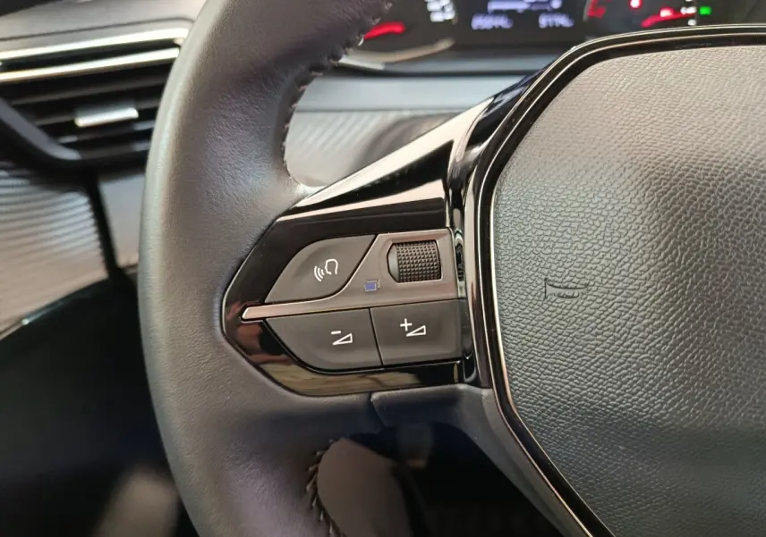 Gros plan sur le volant cuir noir multifonctions côté gauche du Peugeot 208 blanc, avec commandes audio intégrées.