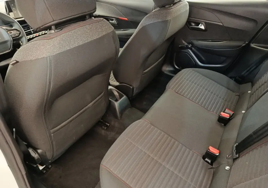 Vue intérieure arrière droite de la Peugeot 208 blanche 2022, sièges tissu gris avec surpiqûres rouges et rangements dos sièges.