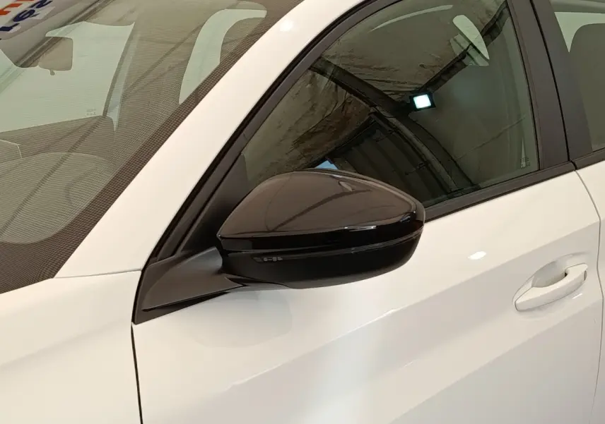 Vue rapprochée du côté gauche avant d'une Peugeot 208 blanche avec rétroviseur noir brillant et poignée de porte blanche.