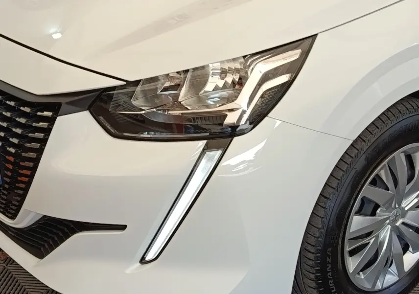 Gros plan sur l'avant droit blanc d'une Peugeot 208 2022, mettant en valeur le phare LED et la roue.