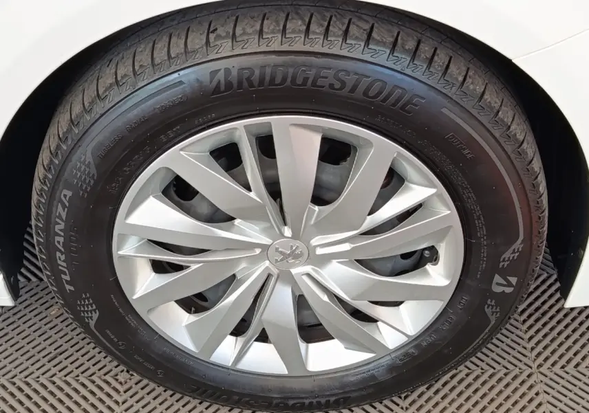Gros plan sur la roue avant droite d'une Peugeot 208 blanche avec jante alliage et pneu Bridgestone Turanza.