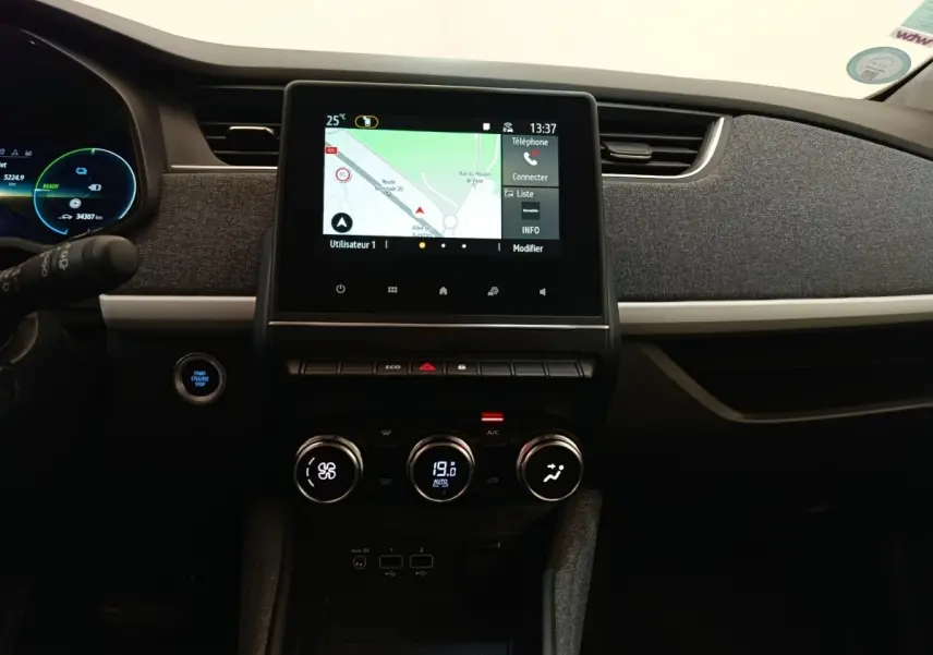 Vue intérieure centrée sur la console centrale de la Renault ZOE blanche 2023 avec écran tactile et commandes climatisation.