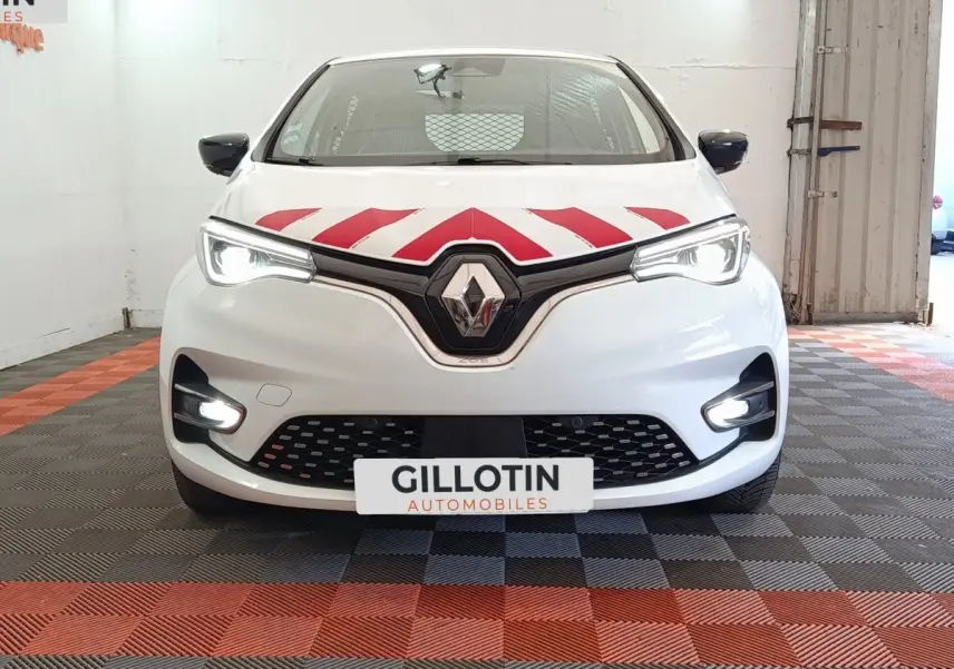 Vue avant d'une Renault ZOE blanche avec bandes rouges diagonales sur le capot et phares LED allumés dans un garage.