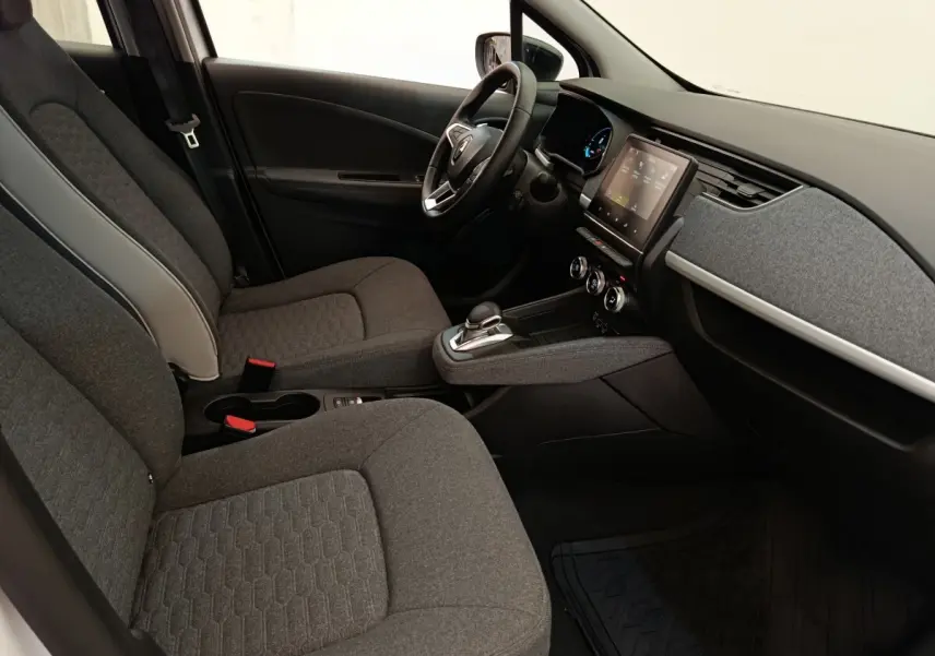 Vue intérieure côté conducteur de la Renault ZOE blanche 2023, avec tableau de bord moderne et sièges gris tissu.